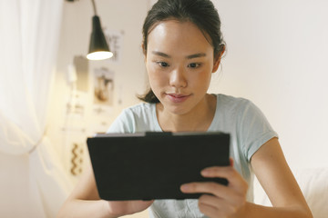 Naklejka premium Asian woman lying on bed and using digital tablet in the night.