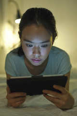 Young asian woman lying on bed and using digital tablet.