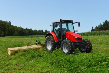 Organic farmer in tractor mowing clover field with rotary cutter