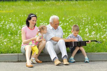 Grandfather playing guitar to his daughter and grandchildren. 