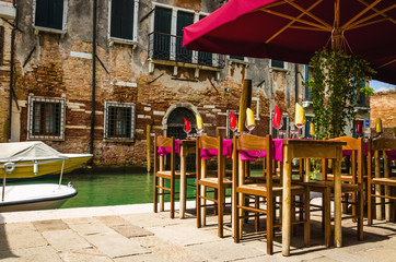 Restaurant on venetian canal among old houses in Venice, Italy.