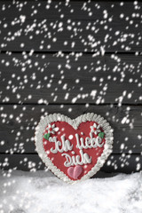 Lebkuchenherz auf Schnee vor Holzhintergrund