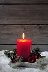 Adventsgesteck mit roter Kerze auf Schnee vor Holzhintergrund