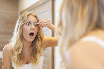 Scared woman tweezing eyebrows in bathroom