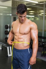 Fototapeta na wymiar Muscular man measuring waist in gym