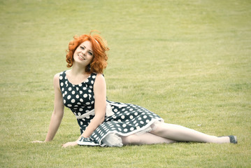 Fototapeta premium Smiling redheaded girl sitting on the grass and smiling