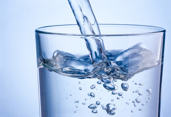 Close-up pouring water into glass on a blue background