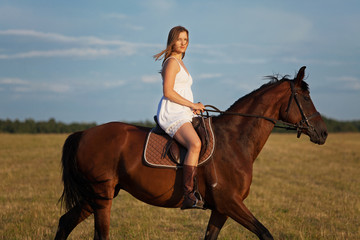 Woman in dress riding on a brown horse