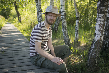 Man wearing a hat sitting on the bridge in the wood