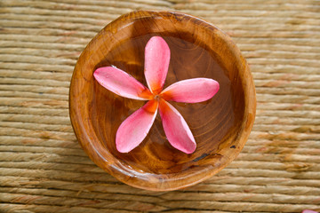 Fototapeta na wymiar Pink frangipani in water wooden bowl on Brown straw mat
