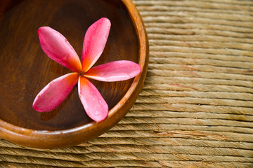 Pink frangipani in water wooden bowl on Brown straw mat