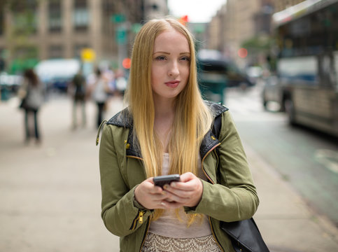Young caucasian blond woman in city texting cellphone