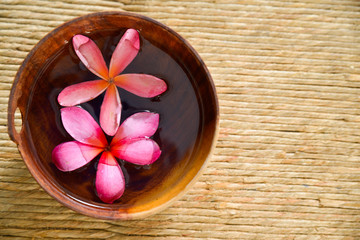 Two Pink frangipani in water wooden bowl on Brown straw mat