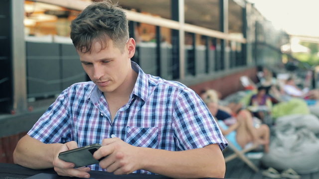 Young man texting, using smartphone in outdoor bar