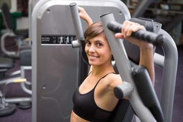 Fototapeta na wymiar Happy brunette using weights machine for arms