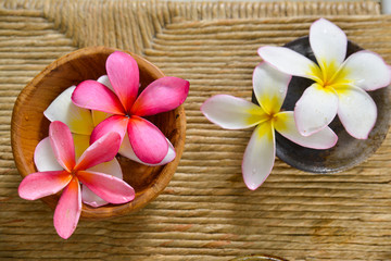 Fototapeta na wymiar White and pink frangipani in bowl and Brown straw mat texture