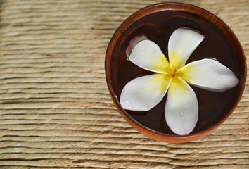 Fototapeta na wymiar frangipani flower in water wooden bowl on Brown straw mat