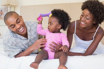 Happy parents playing with baby girl on bed together