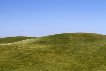 Deurstickers Heuvel Uitzicht op kale groene heuvels met een blauwe lucht.