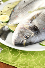 Two fish dorado with lemon on plate on wooden table close-up