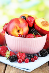 Peaches and berries in bowl on table on natural background