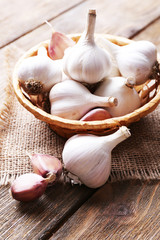 Fresh garlic in wicker basket, on wooden background