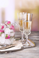 Ice cubes with rose flowers in glass bucket and two glasses