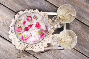 Fototapeta na wymiar Ice cubes with rose flowers in glass bucket and two glasses