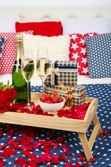 Romantic still life with champagne, strawberry and roses on bed