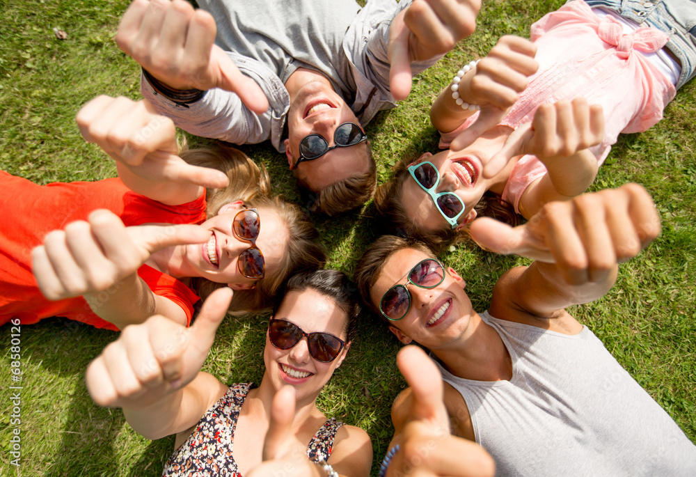 Canvas Prints smiling friends showing thumbs up lying on grass