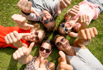 smiling friends showing thumbs up lying on grass