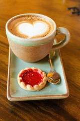 Cup of coffee, heart shape with strawberry biscuit on wood