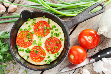 iron frying pan with scrambled eggs and tomatoes on wooden rusti