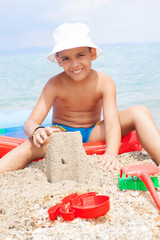 Little boy at tropical beach making sand castle