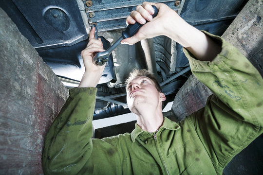 Mechanic tightening with ratchet under car platform
