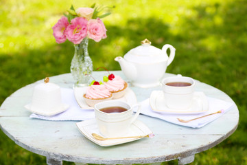 Coffee table with teacups and tasty cakes in garden