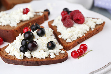 Bread with cottage cheese and berries on wooden tray close-up