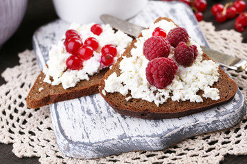 Bread with cottage cheese and berries on wooden board close-up