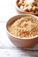 Brown sugar cubes and crystal sugar in bowl on wooden