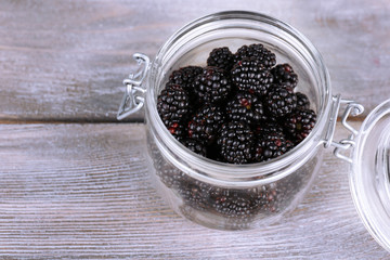Sweet blackberries in glass jar on wooden background