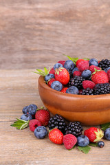 Ripe sweet different berries in bowl, on old wooden table