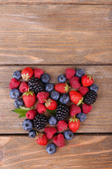 Heart of ripe sweet different berries, on old wooden table