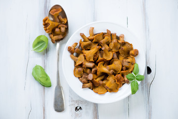 Glass plate with marinated chanterelles and green basil leaves