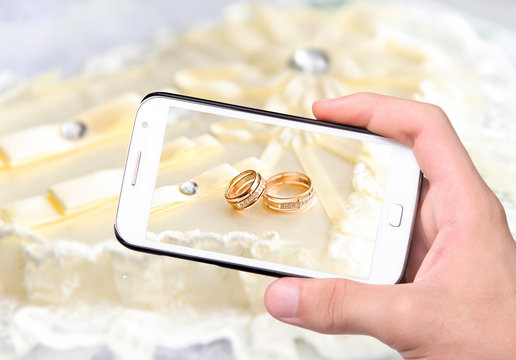 Hands taking photo wedding rings with smartphone
