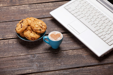 cookie and cup of coffee with laptop on wooden table.