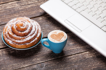 bun and cup of coffee with laptop on wooden table.