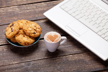 cookie and cup of coffee with laptop on wooden table.