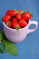 Ripe sweet strawberries in mug  on color wooden background