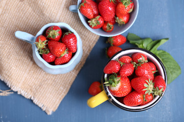 Ripe sweet strawberries in mug  on color wooden background