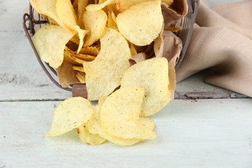 Tasty potato chips in metal basket on wooden table
